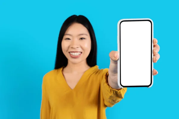 亚洲女人手中拿着白色空屏幕的现代手机 笑容可亲的漂亮中国女士展示出巨大的商机或最新的移动应用 与蓝色工作室背景隔离 — 图库照片