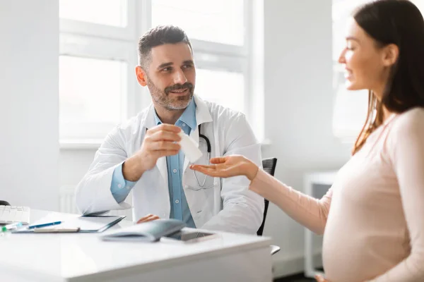 医学和怀孕概念 男妇科医生在医院预约期间给面带微笑的孕妇吃药 探访医生的概念 — 图库照片