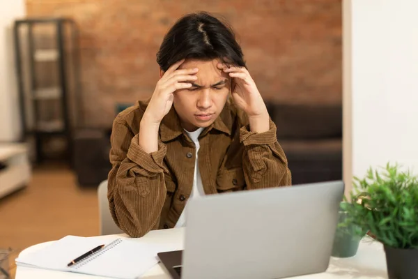 青少年头痛的问题 亚洲学生男子触觉头晕脑胀因偏头痛 厌倦了坐在笔记本电脑前 坐在办公桌前 教育和健康问题概念 — 图库照片