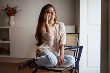 Gülümseyen milenyum melez kadın çağrıları telefonla, konuşur, sandalyeye oturur odanın içindeki boş alana bakar. Dedikodu, uzaktan iletişim, sadece evde iyi haberler.