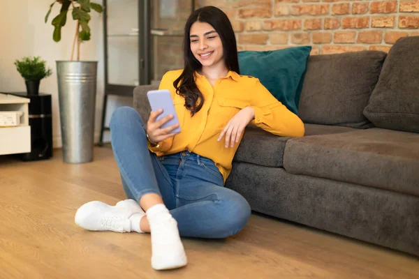 Spanning Tienerdame Met Smartphone Zittend Vloer Door Een Bank Woonkamer — Stockfoto