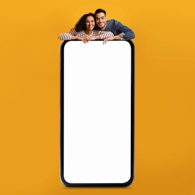 Cep telefonu reklamı. Beyaz ekranlı, sarı ekranlı, internet üzerinden teklif sunan veya uygulama tasarımı yapan Arap erkek ve kadın büyük boş akıllı telefona yaslanan mutlu bir orta doğu çifti.