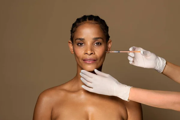 中年黑人妇女使用透明质酸填料 去除仿皱纹 站在棕色工作室背景 复制空间的肖像 — 图库照片