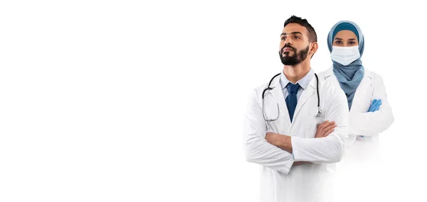 阿拉伯男医生和女医生 身穿制服 因白人背景而被隔离 专业的穆斯林医务工作者 手挽手站立 随时可接受治疗 头脑发热 有复制空间 — 图库照片