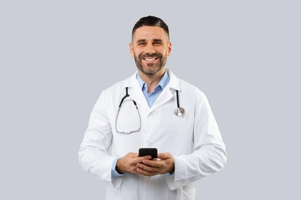 Retrato Terapeuta Masculino Amigável Casaco Branco Com Estetoscópio Usando Smartphone — Fotografia de Stock