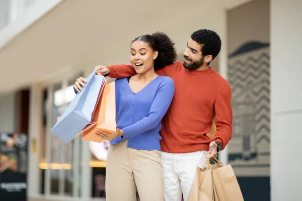 stock image Family Shopping Offer. Husband Giving Paper Shopper Bags To Excited Wife Surprising Her Standing Outdoors. Mixed Couple Buying New Clothes Together On Weekend. Seasonal Sale Concept