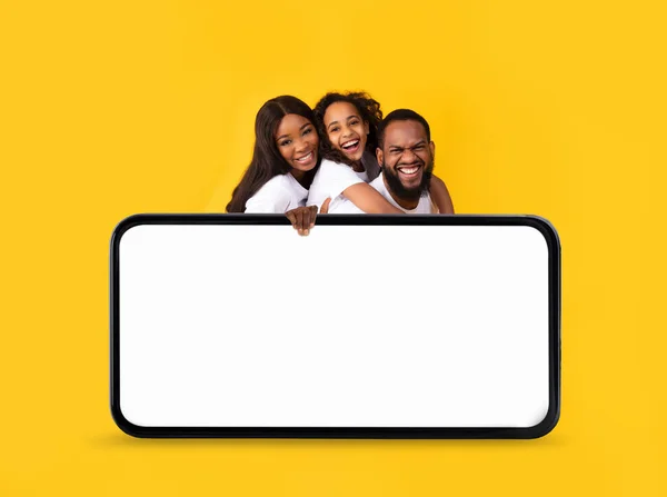 Sorrindo Família Negra Três Espreitando Atrás Big Blank Smartphone Sobre — Fotografia de Stock