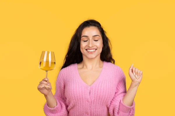 幸せは黄色のスタジオの背景に隔離された願いを作る ワインのガラスを保持目を閉じた若い白人のブルネットの女性にインスピレーションを与えました 休日のお祝いや人々の感情 — ストック写真