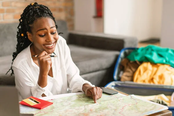 快乐的非洲裔美国女人看着地图 为旅行做准备 并为将来的旅行查看最佳路线 快乐的女士选择旅行的目的地 客厅的内部 — 图库照片