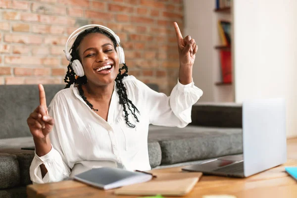 ノートパソコンの前の机に座って ワイヤレスヘッドセットを使用して 仕事から休憩しながら音楽 ダンスを楽しみ スペースをコピーする楽しいアフリカ系アメリカ人女性 — ストック写真