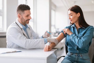 Genç Avrupalı kadın koronavirüse karşı aşı oluyor, orta yaşlı erkek doktor kadın omzuna iğne yapıyor, kliniğin içinde oturuyor, boşluğu kopyalıyor.