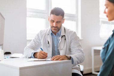 Sağlık sigortası, sağlık kontrolü. Bayan ziyaretçi doktor, erkek pratisyen doktor kişisel bilgiler yazıyor, form dolduruyor veya tedavi için reçete yazıyor