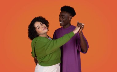 Romantik, çok kültürlü genç çiftler, kırmızı stüdyo arka planında vals yapıyorlar. Mutlu, obez, İspanyol bir bayan, yakışıklı, Afro-Amerikan erkeğiyle eğleniyor.