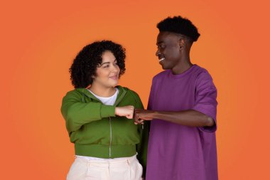 Mutlu gülümseyen genç bir çift Afro-Amerikan erkek ve obez İspanyol kadın yumruk tokuşturuyor ve birbirlerine gülümsüyorlar, işbirliği ve takım çalışması konsepti, kırmızı stüdyo geçmişi
