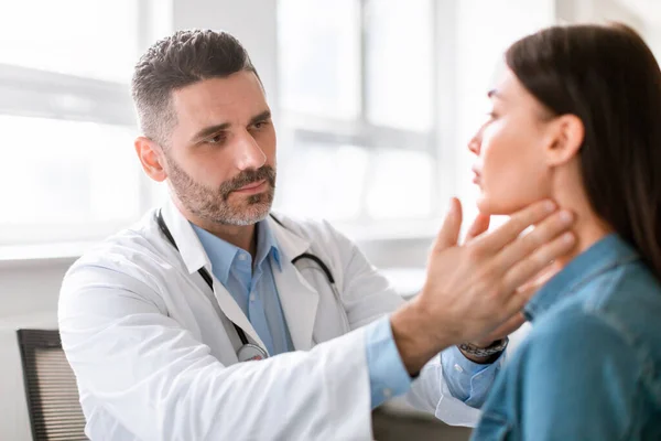 Medicine, healthcare and medical check up concept. Male doctor checking patients tonsils at hospital. Endocrinologist examining throat of young lady in clinic