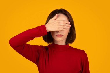Görmek bile istemiyorum. Güzel, beyaz bir kadın, kırmızı bir süveter giyiyor. Elle gözlerini kapatıyor. Turuncu stüdyo arka planında izole edilmiş.