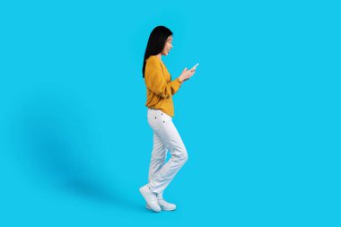 Profilde, akıllı telefon kullanan, mavi arka planda gülümseyen, cep telefonlu, kısa boylu Asyalı genç bir kadının cep telefonu uygulamasındaki erkeklerle sohbet ettiği,