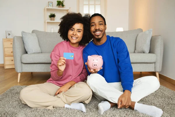 快乐的黑色情侣展示信用卡和Piggybank与家庭储蓄坐在地板上 微笑相机 配偶广告大银行的报价 财务安全概念 — 图库照片