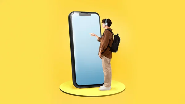 男生使用大型智能手机 带空白屏幕 背着背包站在黄色工作室背景上 男子触摸电话触摸屏广告教育应用程序 — 图库照片