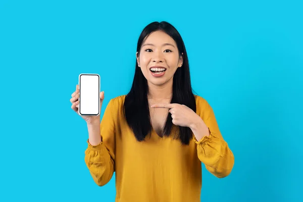 韩国女人手中拿着白色空屏幕的现代智能手机 快乐而年轻的亚裔女士展示出很好的报价或最新的移动应用 在蓝色工作室背景下被隔离 是个笑柄 — 图库照片