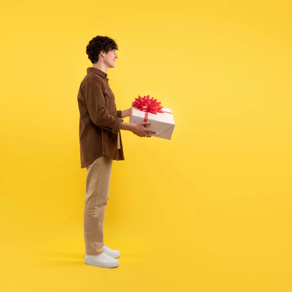 送货上门 快乐的年轻人抱着礼品盒鞠躬问候站在黄色工作室背景下的人 的侧视图 正方形 — 图库照片