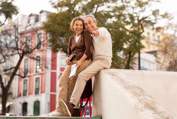 在新城市里 快乐成熟的配偶会在相机前指指指点点手指 然后坐在外面 带着旅游地图旅行和散步 资深旅游人士享受假期及退休生活 — 图库照片