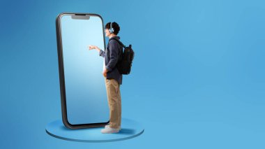 Mavi Stüdyo Arkaplanı üzerinde sırt çantalı, kulaklık takan, geniş cep telefonu dokunmatik ekranlı bir adam görüntüsü. Metin için Boş Alan, Tam Uzunlukta Panorama