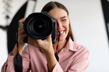 Elinde fotoğraf makinesi olan mutlu genç kadın fotoğrafçı ışıklandırma ekipmanları, seçici odak, yakın çekim, kopyalama alanı ile fotostudio 'da çalışıyor.