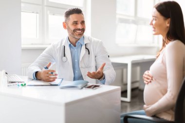 Hamile bir kadın klinikte doktor ziyareti yapıyor. Terapist, mutlu bir bayana tavsiyelerde bulunuyor. Hamilelik süresince sağlık hizmetleri