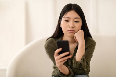 Sıkıcı genç Asyalı kadın, gündelik kıyafetleriyle evde oturuyor, akıllı telefon kullanıyor, internetten güzel içerikler arıyor, erkek arkadaşından telefon bekliyor, kendini yalnız hissediyor, fotokopi çekiyor, yakın çekim yapıyor.