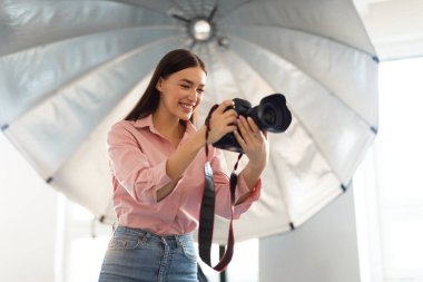 Genç bayan fotoğrafçı yansıtıcı şemsiyenin önünde duruyor, modern fotostudio 'da profesyonel dslr kamera ile çalışıyor, serbest alan