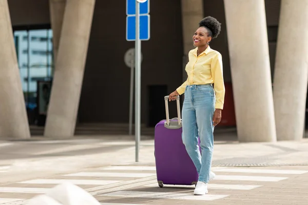 stock image Happy African American Tourist Woman Walking On Crosswalk Arriving At Airport Posing With Travel Suitcase. Full Length Shot Of Female Passenger Walking With Her Luggage Near Station Outside