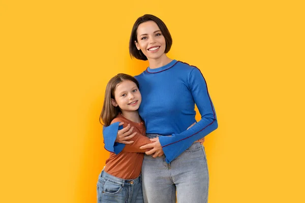 stock image Mothers Love Concept. Portrait of happy young mom embracing her cute preteen daughter, happy loving family mommy and child standing isolated over yellow studio background, copy space