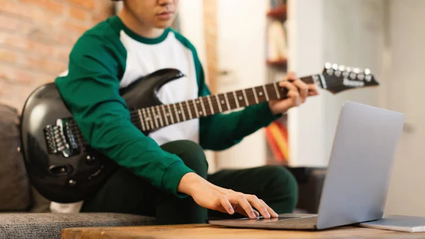 Cropped Shot Of Teen Guy Playing Electric Guitar And Using Laptop Learning Musical Instrument Online Sitting At Home. Technology And Music Concept. Selective Focus, Panorama