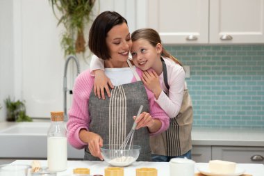 Beyaz tenli genç anne ve önlüklü küçük kızın kurabiye, sarılma ve mutfak içinde eğlenceli, lezzetli hobileri olmasına sevindim. Birlikte yemek pişirmek, ev yapımı tatlılar.