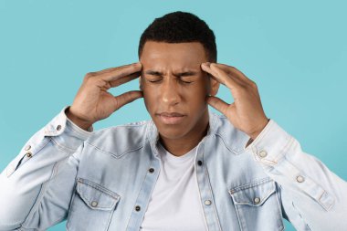 Bin yıllık üzgün, gözleri kapalı, baş ağrısı ve stresten muzdarip siyahi bir adam. Mavi stüdyo arka planında izole edilmiş olduğunu düşünüyor. Sağlık sorunları, migren, beyin fırtınası ve yoğun duygular.