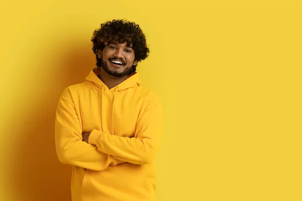 穿着黄色连帽衫的快乐英俊的千年印度人 双手交叉在胸前对着摄像机微笑 在黄色工作室的背景上独自摆姿势 复制广告空间 — 图库照片