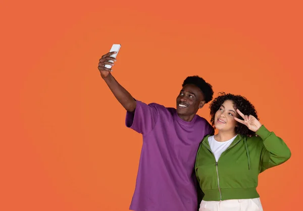 stock image Cute cheerful loving multiethnic young couple black guy and hispanic chubby woman taking selfie together on red studio background, smiling and gesturing, using smartphone, copy space