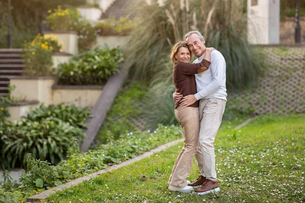 微笑的老年配偶站在绿园的户外拥抱周末 看着相机 老年时的浪漫与爱情概念 成熟约会伴侣的全长镜头 — 图库照片