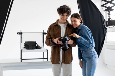 Profesyonel fotoğrafçı ve bayan asistanı modern çantalar için içerik fotoşopu çekerken fotoğrafları kontrol ediyorlar.