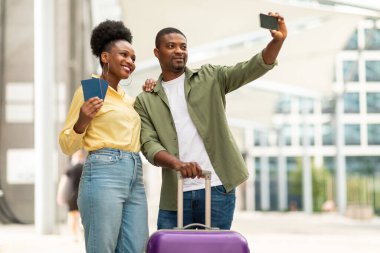 Tatil Selfie 'si. Neşeli siyahi turistler valizli cep telefonu pozu ve pasaportlarıyla dışarıda havalimanında fotoğraf çekiyor. Ulaştırma ve Turizm Konsepti