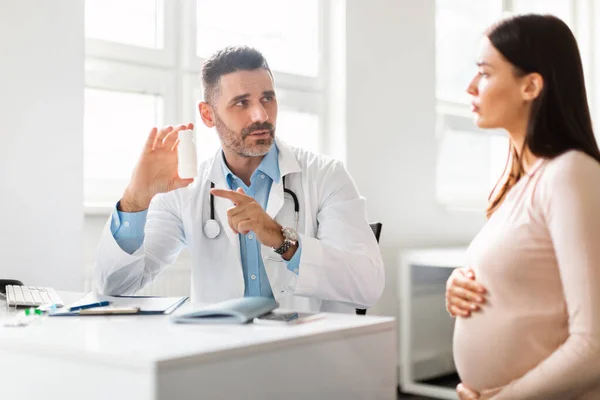 男医生给孕妇开药方 拿着装有药丸的瓶子 指着瓶子 给怀孕的年轻母亲服用维生素 产前护理概念 — 图库照片