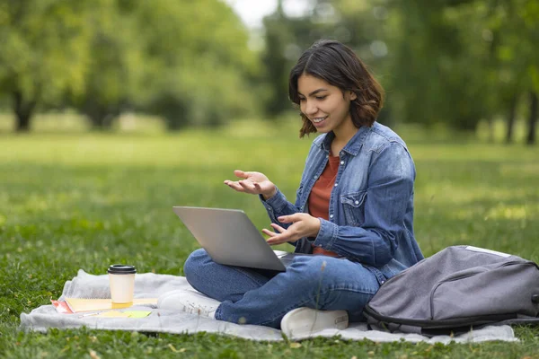 笑顔のアラブ女性学生は キャンパス内でプレイしながらテレビ会議のためにコンピュータを使用してノートパソコンの屋外で 幸せな若い中東の女性にビデオ通話を行い オンライン通信を楽しむ — ストック写真
