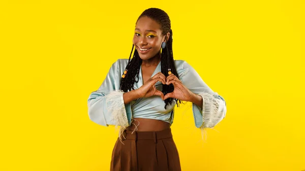爱情签名 快乐的非洲裔美国人女士塑造的手就像心形微笑着拍摄照片有着明亮的化妆站在黄色的工作室背景 情人节浪漫的概念 — 图库照片