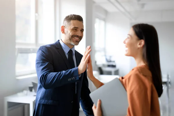 Happy coworkers celebrating achievement in office, man and woman giving high five and smiling, businesspeople enjoying great success, job well done
