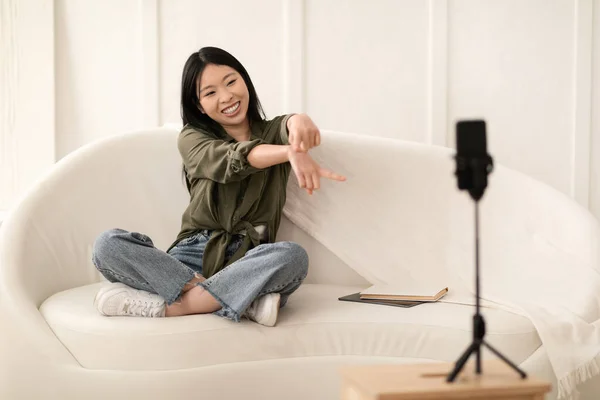 自宅からストリーミング有名なブロガーの若い魅力的な韓国の女性は 女性のインフルエンサーは スマートフォンのカメラとジェスチャーを見て リビングルームでソファに座っている ブログのコンセプト — ストック写真