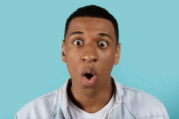 Portrait of shocked surprised funny silly millennial black guy with open mouth looking at camera isolated on blue studio background. Emotions, facial expression reaction to surprise, news, offer