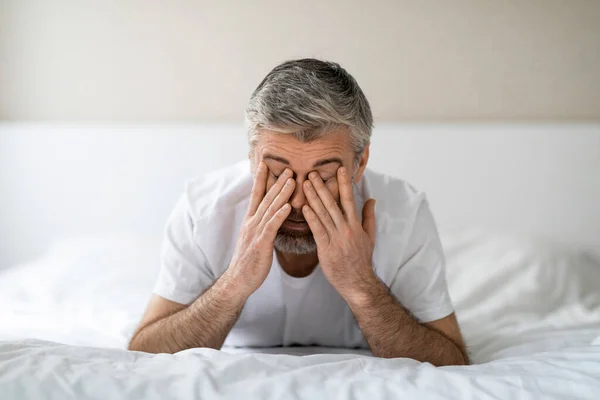 睡眠障害 疲れ切った白髪の中年男性のベッドで朝に横たわって 目をこすり 眠れない夜 白い寝室のインテリア コピースペースの後に疲れて感じて閉じます — ストック写真