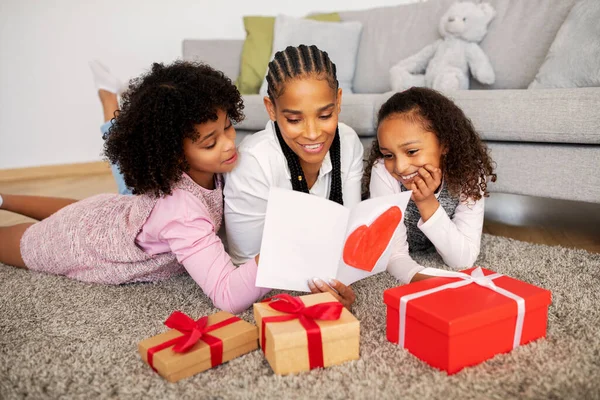 stock image Young Black Mom And Two Daughters Reading Greeting Card On Mothers Day, Kids Congratulating Their Mommy Celebrating Family Holiday Or Her Birthday Lying On Floor Among Wrapped Gifts Boxes At Home