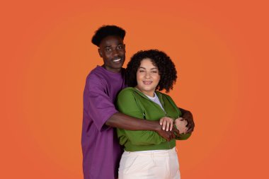 Mutlu, çekici, sevgi dolu, renkli stüdyo geçmişinde poz veren ırklar arası bir çift. Yakışıklı siyah adam güzel kadınına sarılıyor. Sevgi ve şefkat gösteriyor.